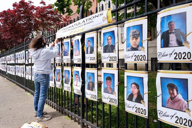 School employee Luz Carlson hangs a sign over pictures of the graduating senior class displayed on the fence at James Madison High School in Brooklyn in May 2020.